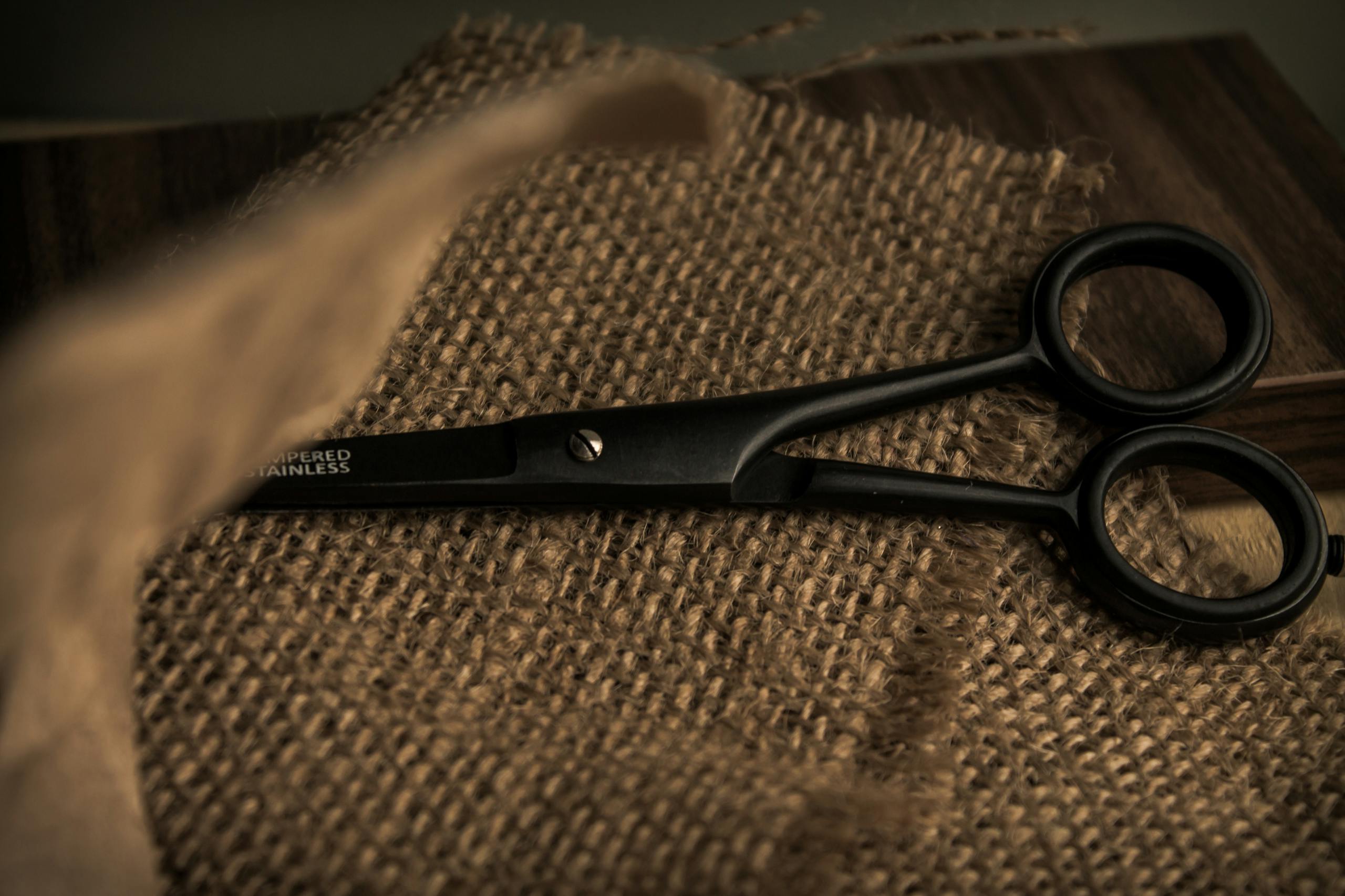 A close-up of black scissors resting on a burlap fabric, conveying a rustic and vintage feel.