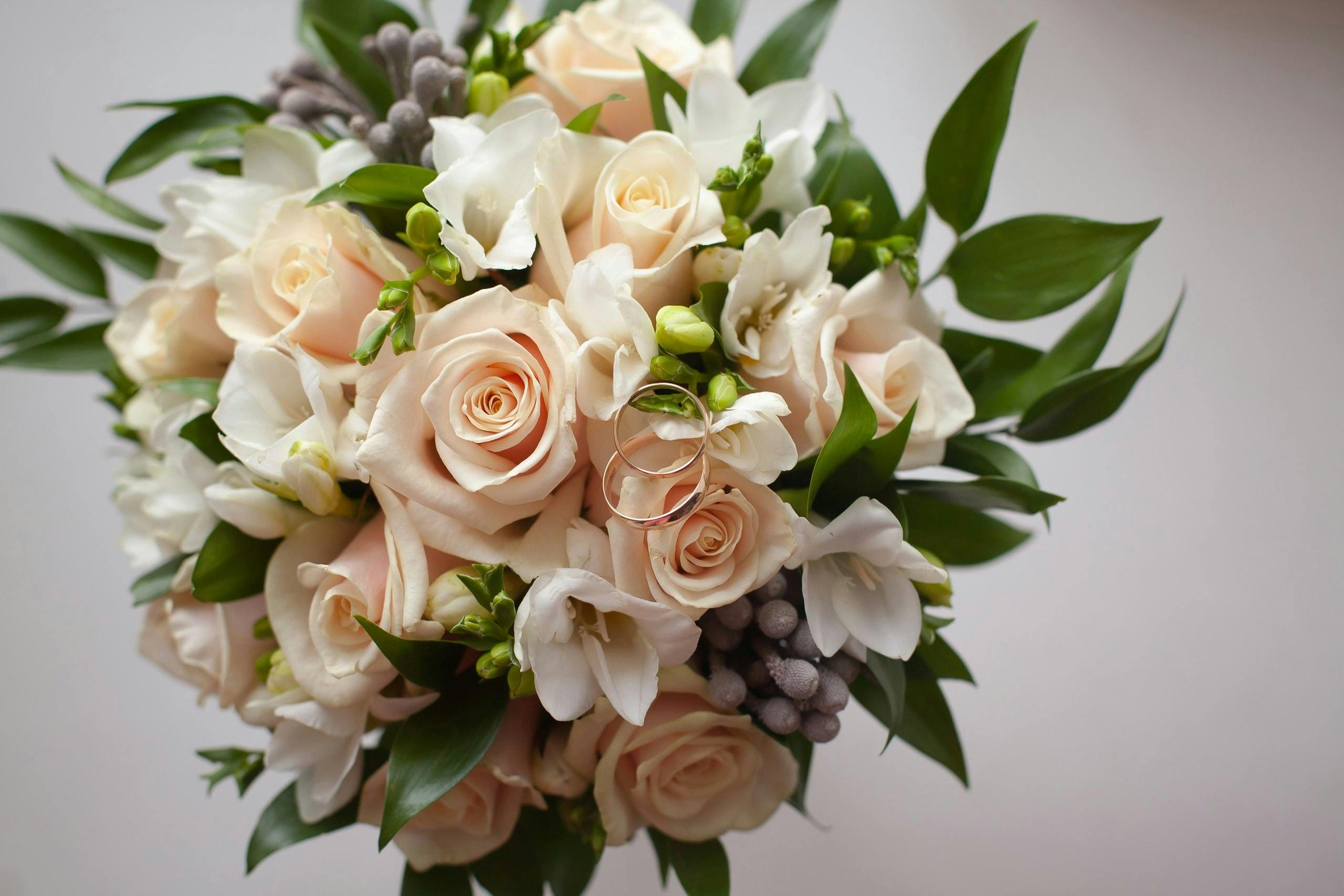 From above of composition of blooming flower bouquet with gentle rose petals and green spiky leaves on white floor