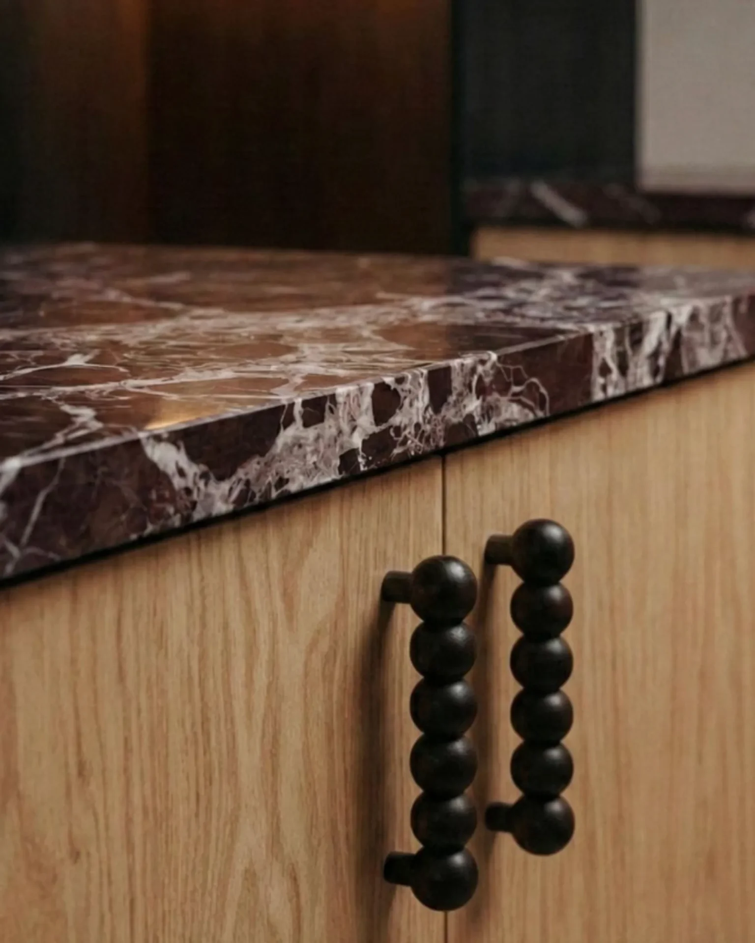 Close-up of a dark brown marble countertop edge above a light wood cabinet, with black bead curtain hanging from the cabinet handles visible beside it.