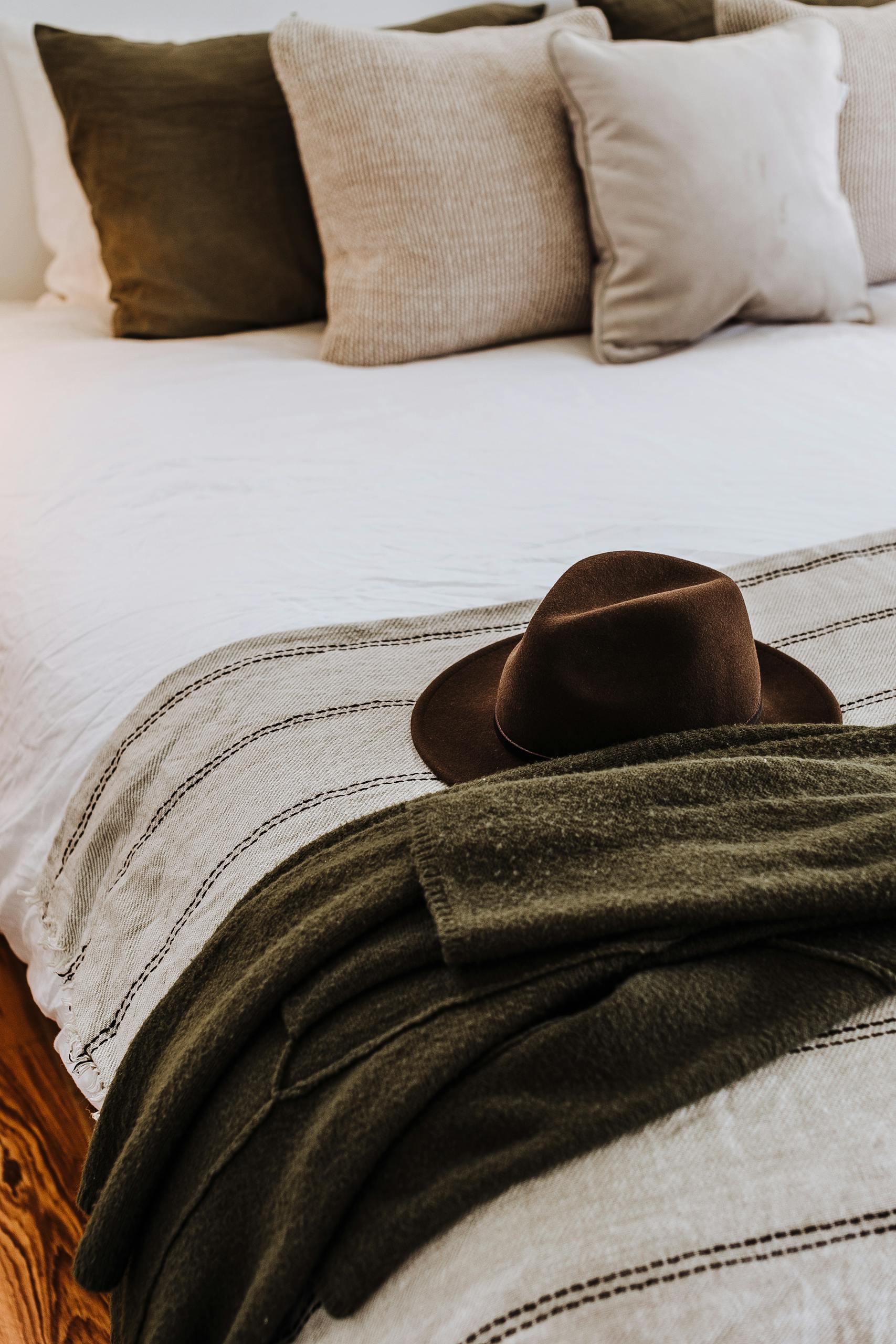 Hat and clothes on ornamental bed cover with assorted cushions in house in daylight